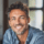 Homme souriant avec chemise en jean, intérieur lumineux.