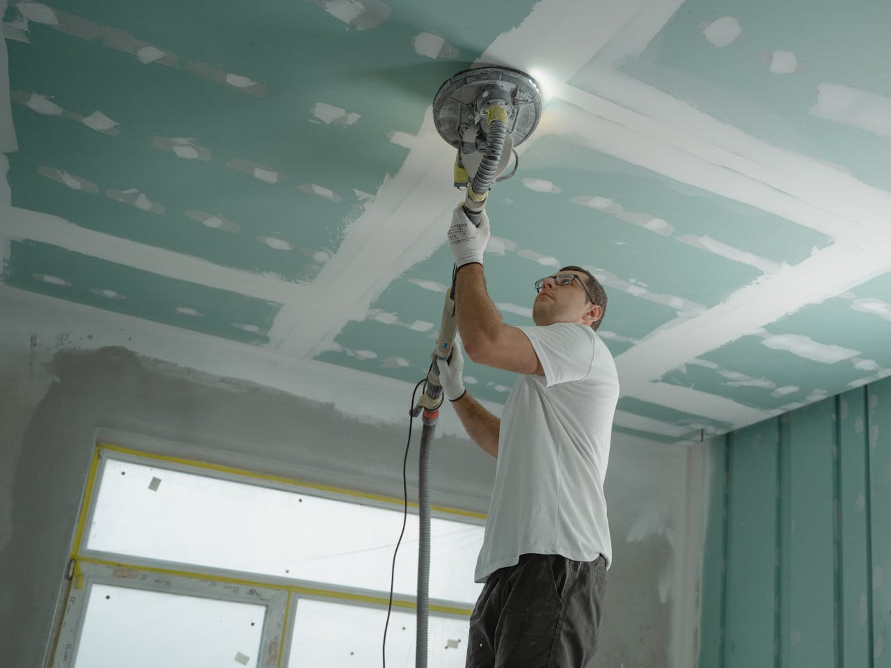 services-01 A professional worker sanding the ceiling during a home renovation project. Indoor construction setting.