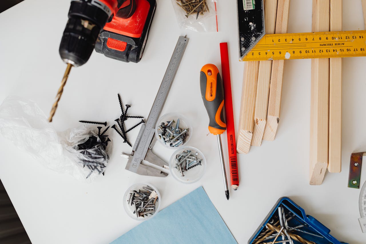 contact-img-01 A collection of carpentry tools including drill, caliper, and try square on a white table.